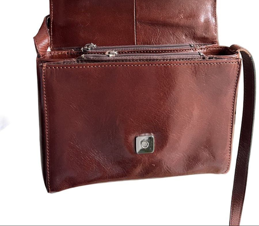 Brown leather crossbody bag held by a hand against a white background