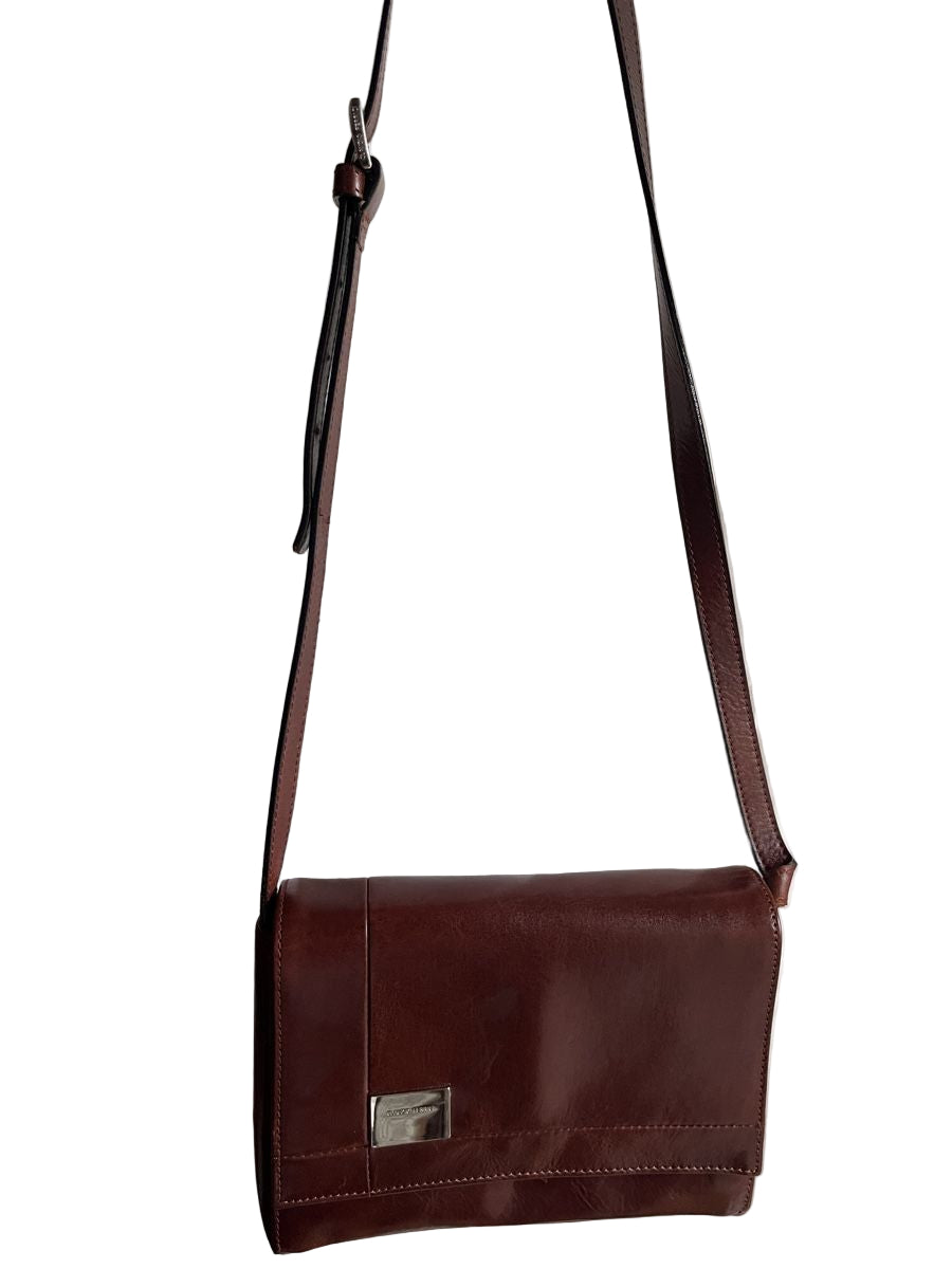 Brown leather crossbody bag against a white curtain background