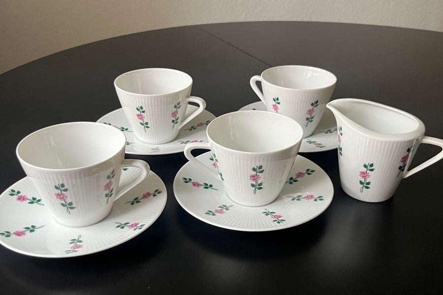 Set of white ceramic tea cups and saucers with floral patterns on a dark surface.
